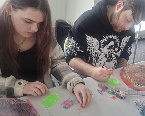 Two young people sat at a table engaging in creative art activities as part of a mental health workshop